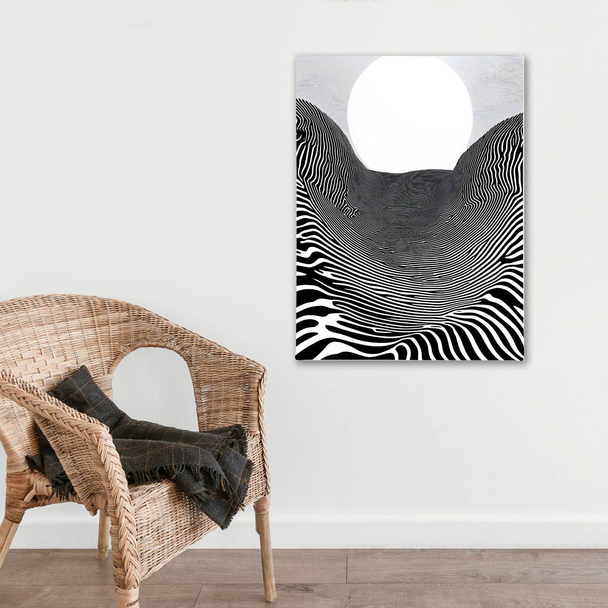 Abstract black and white artwork on a wall above a wicker chair with a blanket.