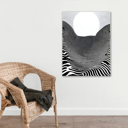 Abstract black and white artwork on a wall above a wicker chair with a blanket.