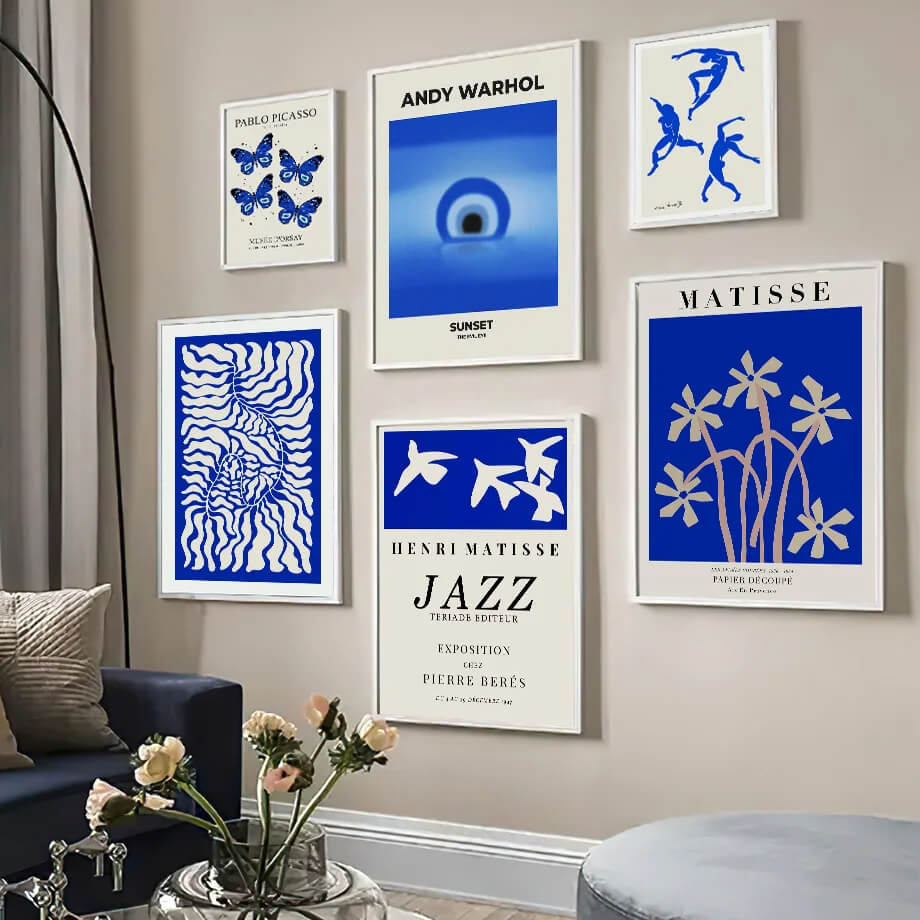 Wall with framed posters featuring artists like Andy Warhol and Henri Matisse, with a couch and flowers in the foreground.