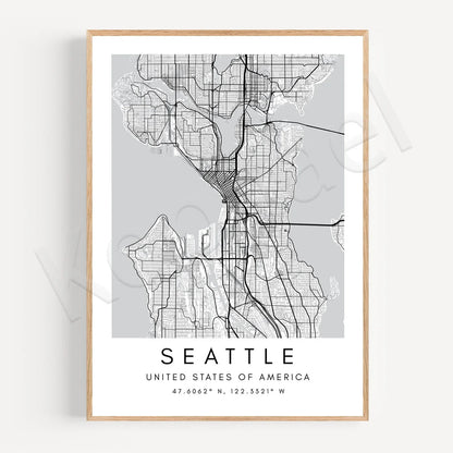 A framed minimalist city map print of Seattle, United States, featuring a black street grid on a light gray background with the city name and coordinates printed below, set in a light wood frame against a white wall.