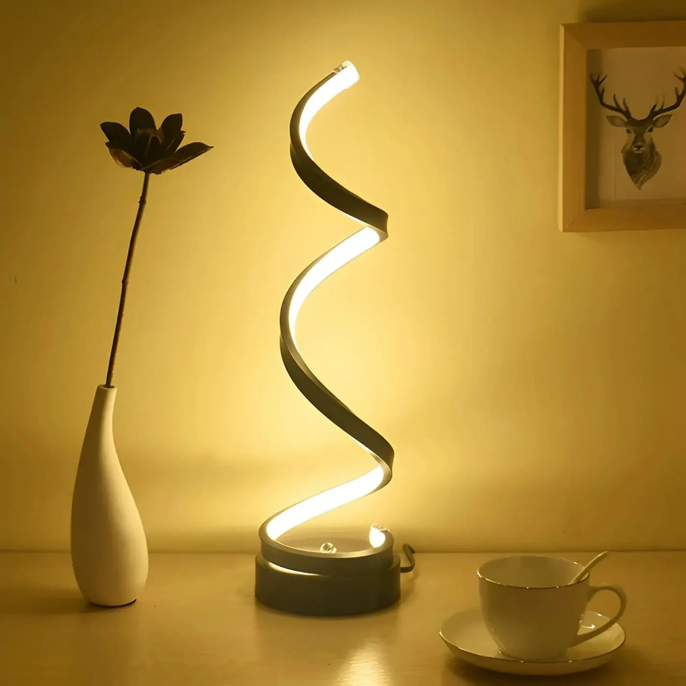 Spiral LED lamp on a table with a vase, cup, and saucer in a warm setting.