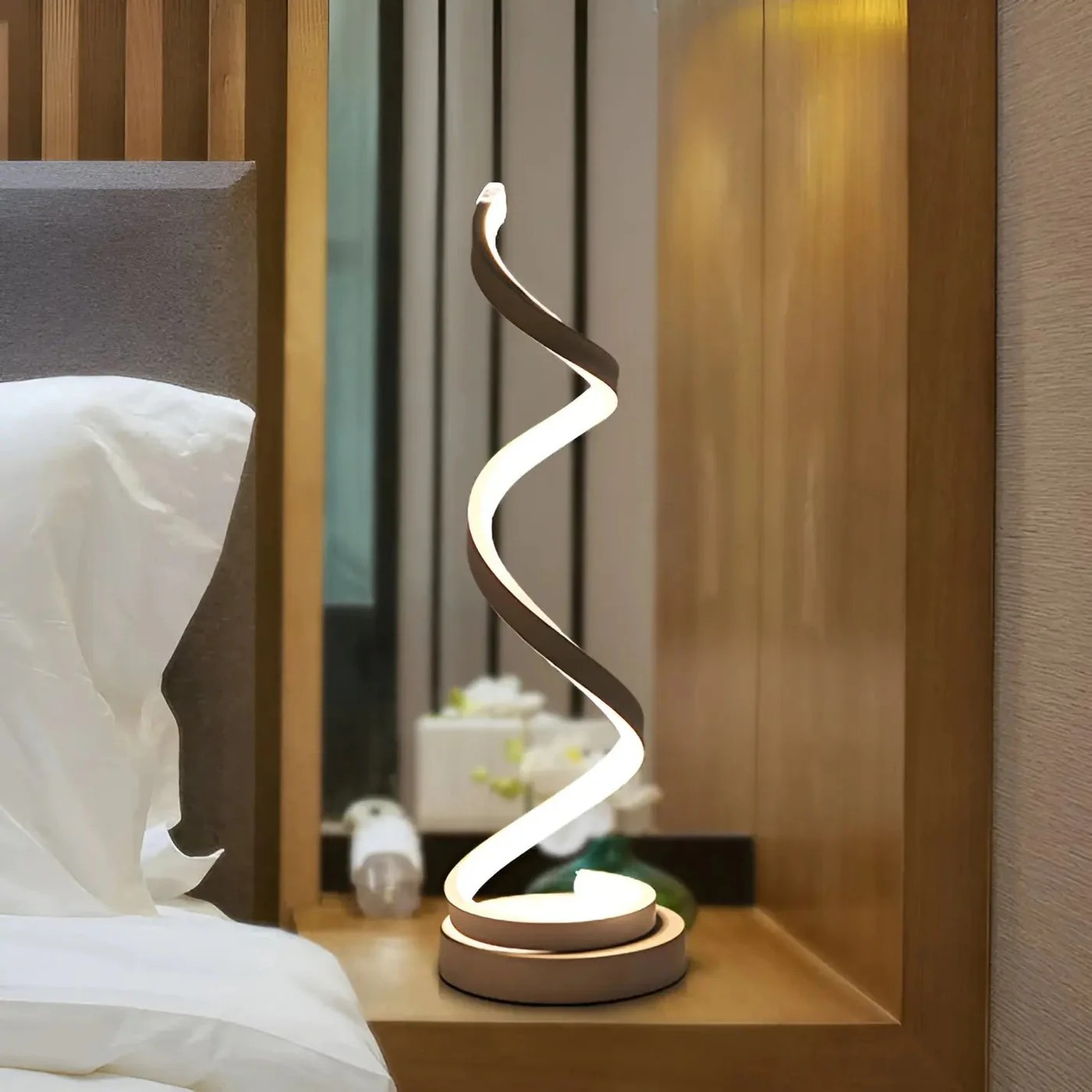 Modern spiral table lamp on a bedside table with a blurred bedroom background