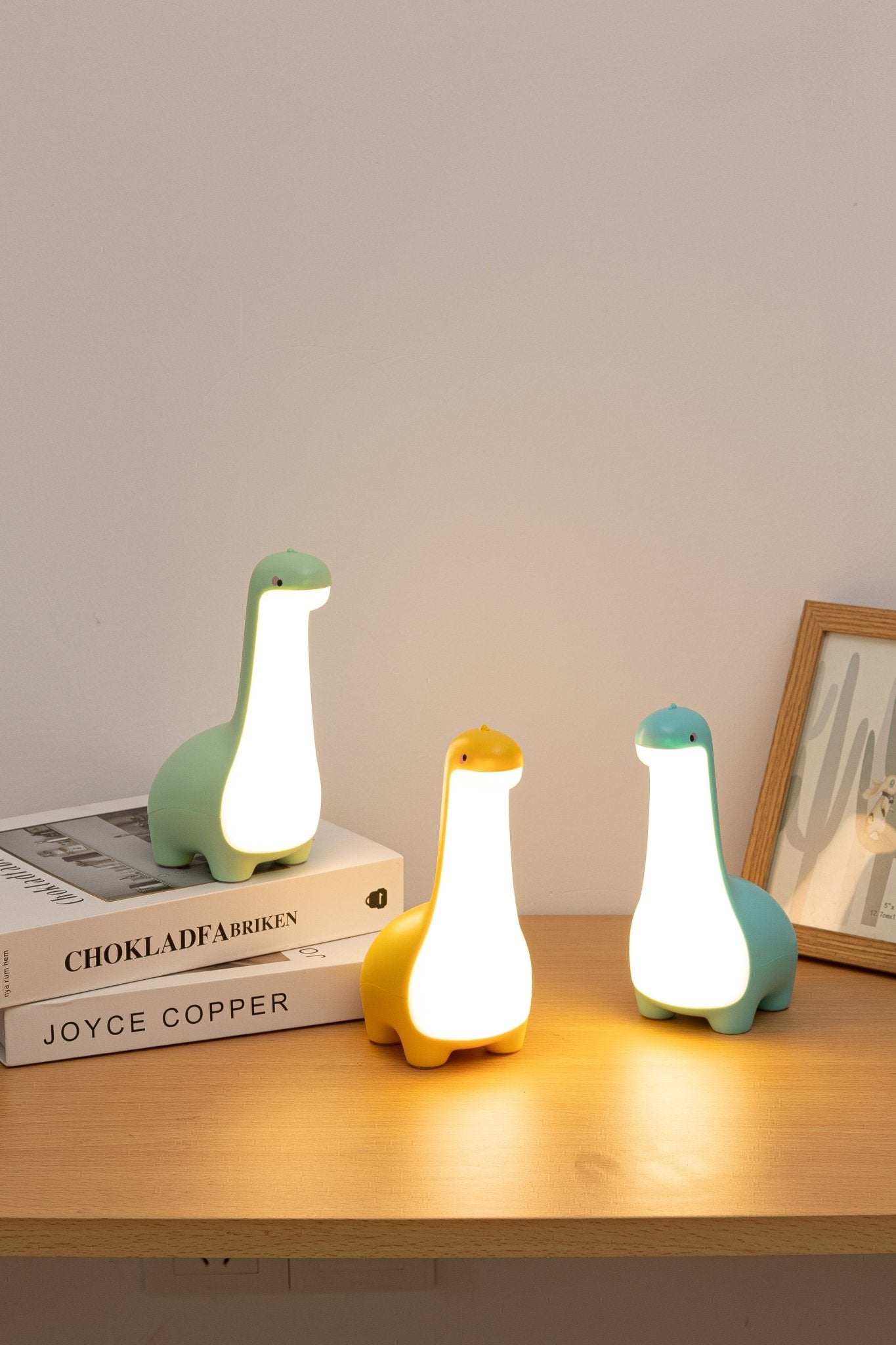 Three dinosaur-shaped night lights on a wooden surface with a neutral background