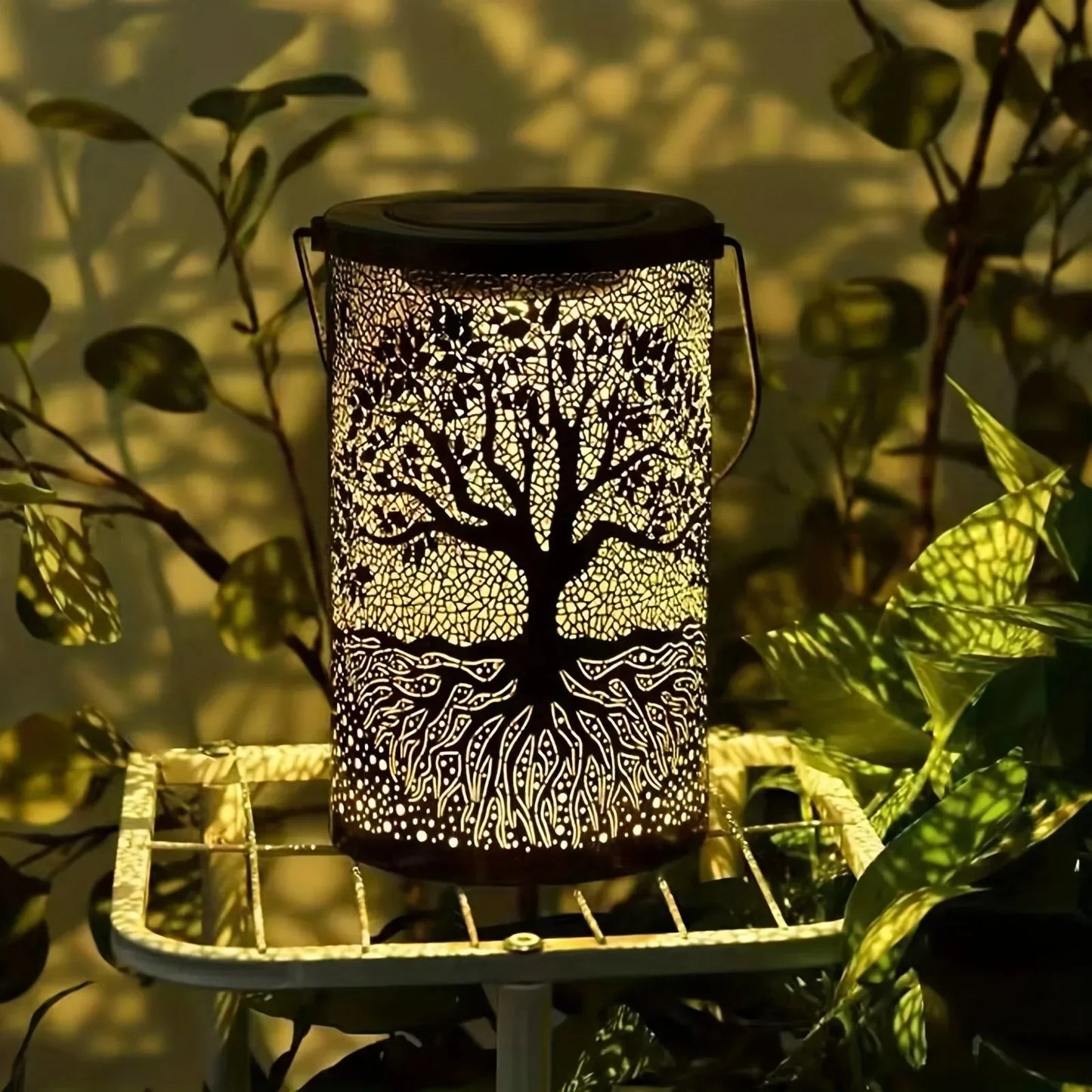 Decorative lantern with tree design on a stand surrounded by plants